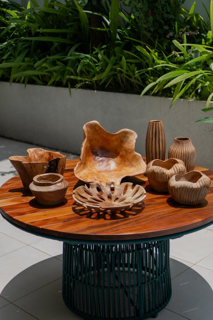 services-01 Wooden bowls and vases on a patio table with lush green plants in the background.